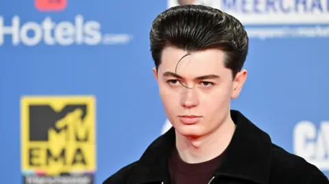 Getty Images Elliot James Reay poses for photographers against a blue branded backdrop at the MTV Europe Music Awards in Manchester in 2024.