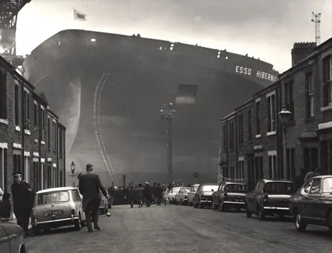 Newcastle City Library Photo of huge ship, Esso Hibernia at the end of street showing houses, cars and people