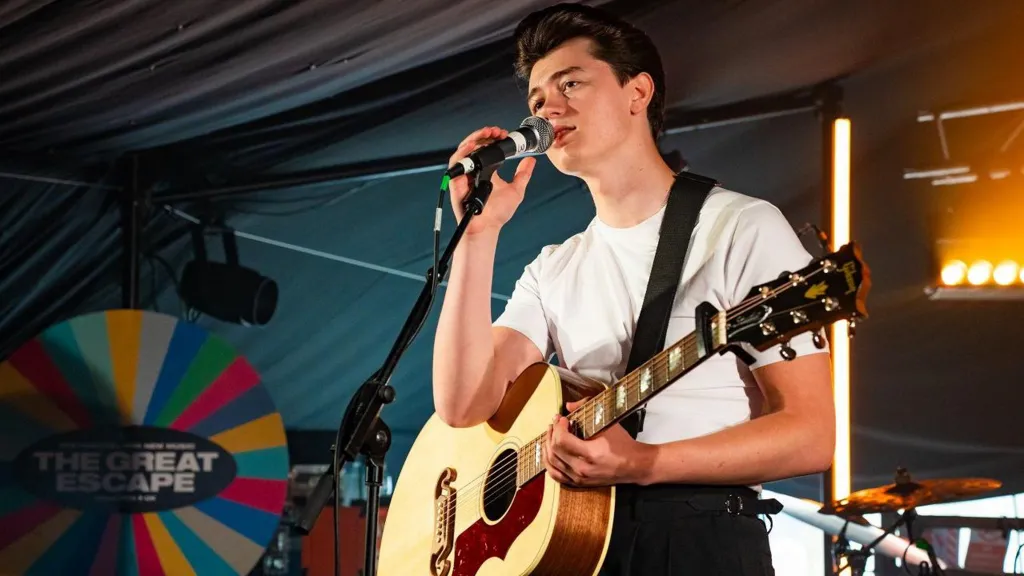 “A young singer from Bury performing a vintage rock ’n’ roll cover while recording a TikTok-style video in a casual setting—his journey from local busking to performing at Graceland.”