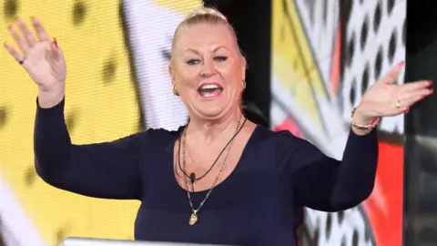 Getty Images Kim Woodburn, in 3rd place, leaves the Celebrity Big Brother house on February 3, 2017. She has a navy top on and is waving at the crowd and smiling.